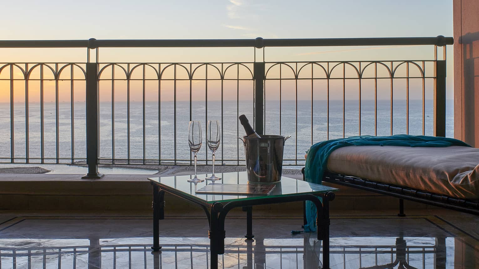 Suite balcony with longue chair, side table with champagne, sea views at sunset