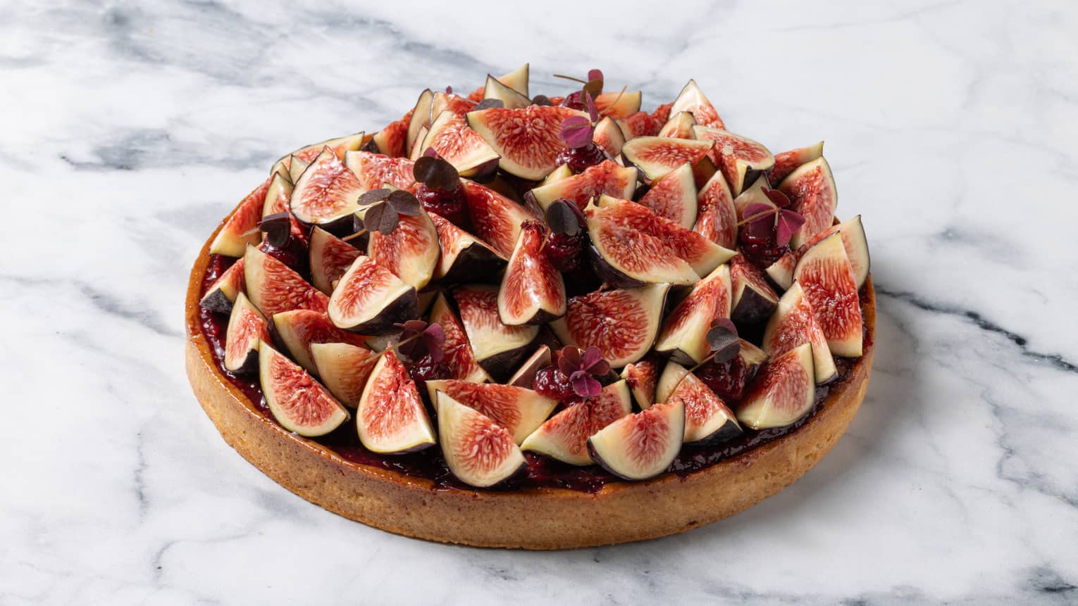 Circular tart mounded with fresh fig wedges on marble surface