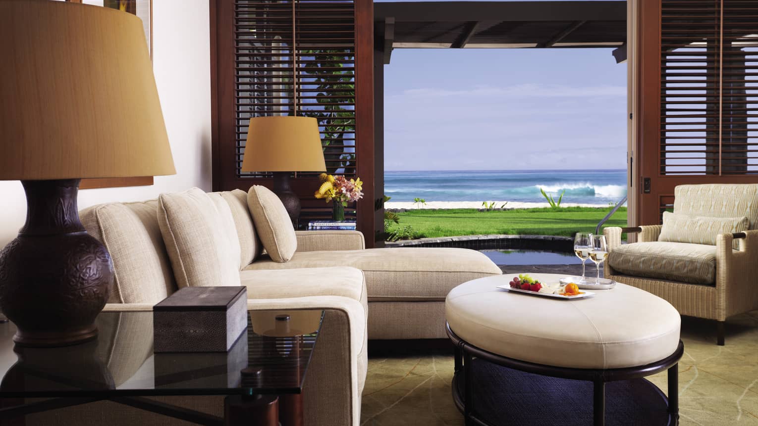 ‘Anelakai Suite plush white chaise, round leather footstool by open wood patio shutters