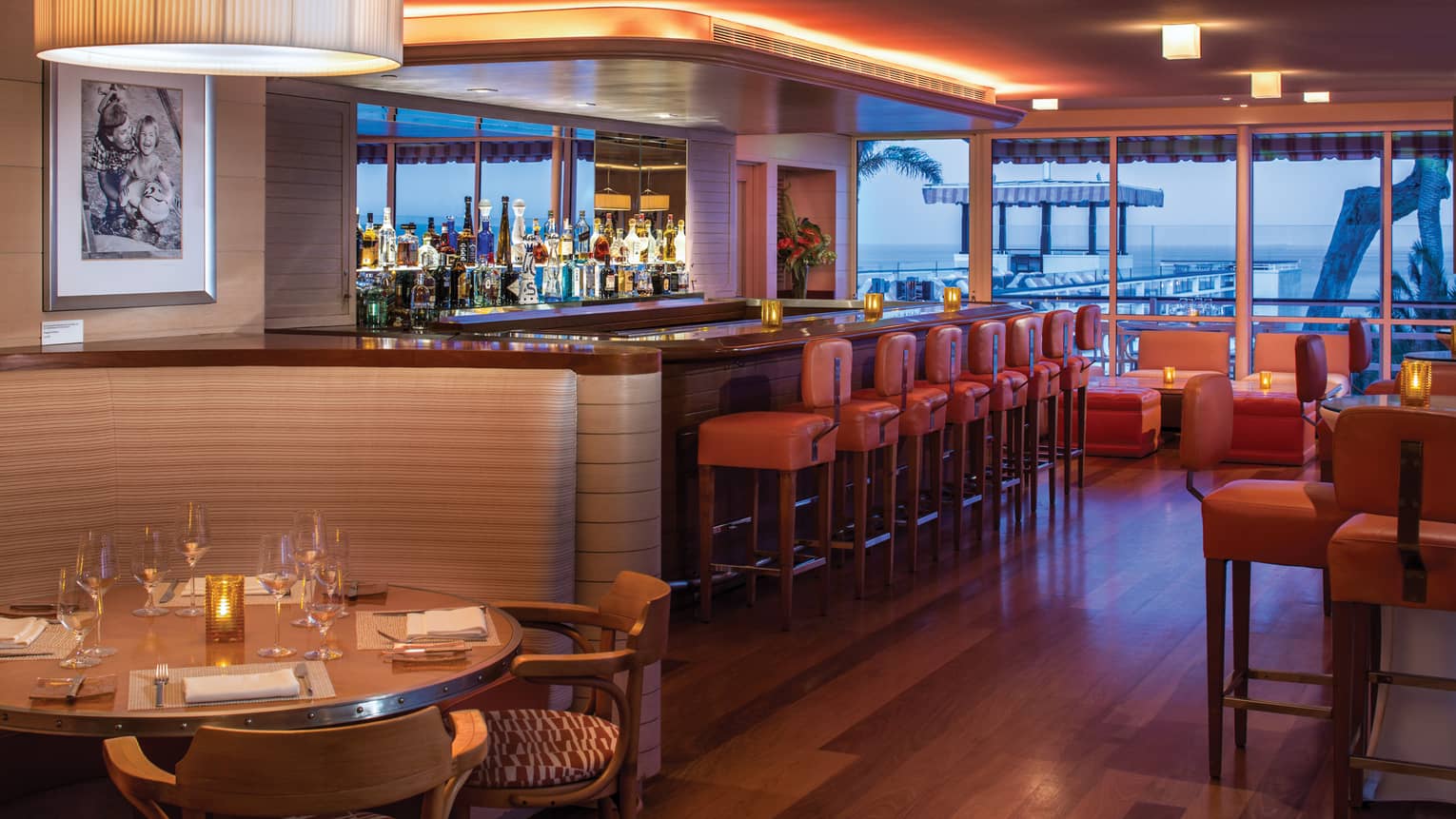 Tydes dining room with orange leather stools along bar, curved candle-lit booth