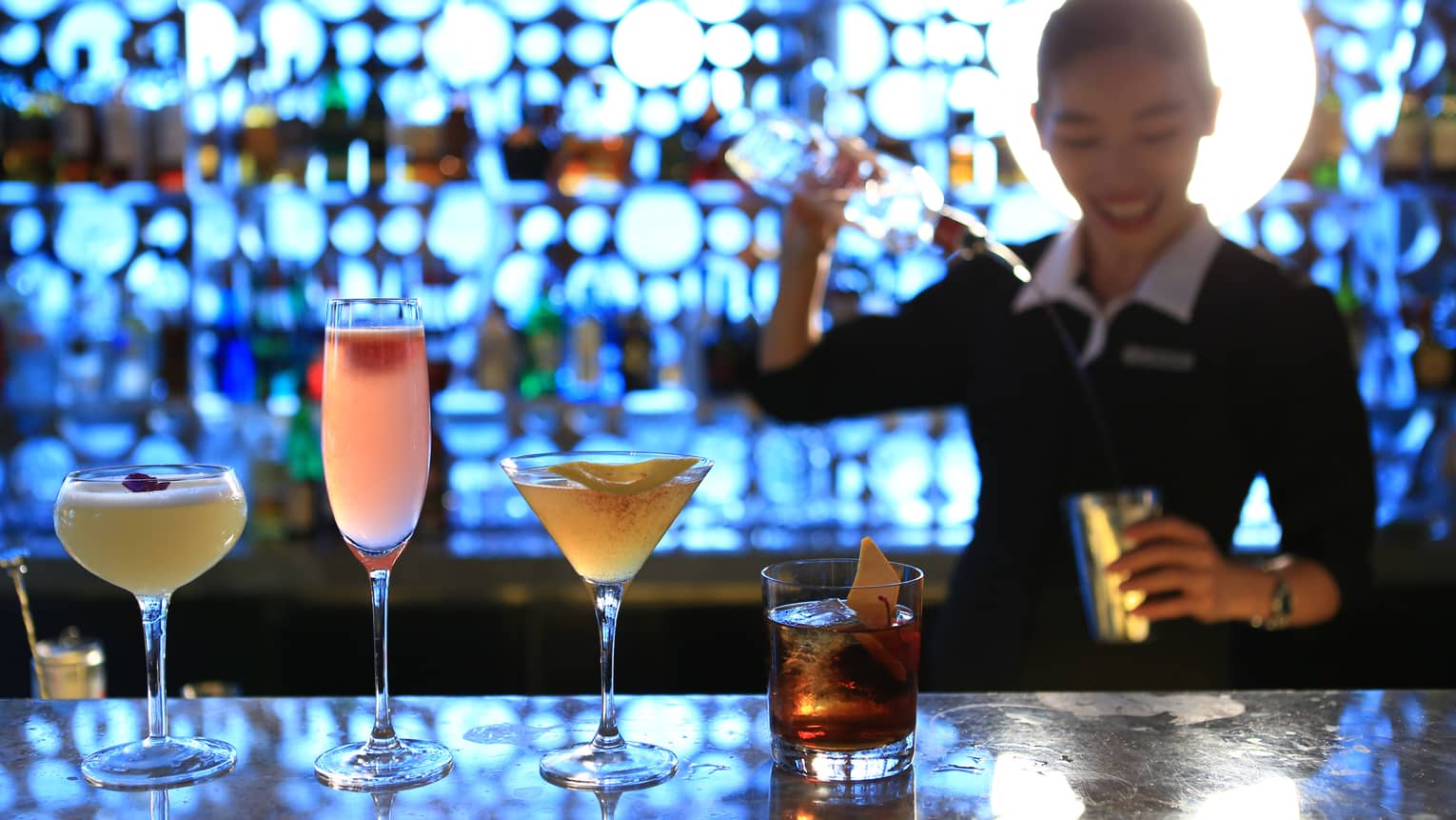 Colourful cocktails in row on Yi bar, bartender mixing drink in background