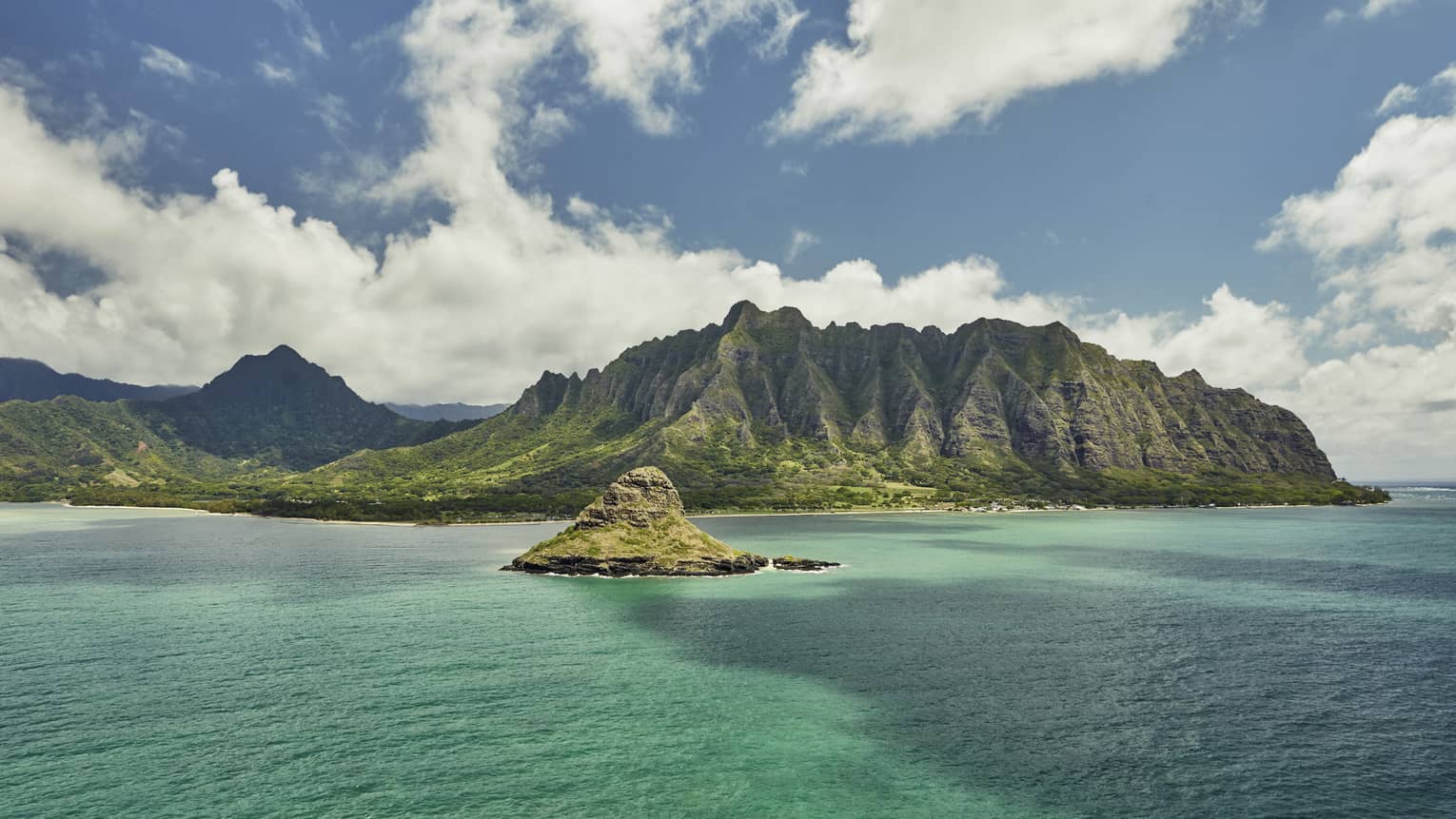 Sweeping green Oahu, Hawaii mountains, small island over turquoise lagoon, white clouds