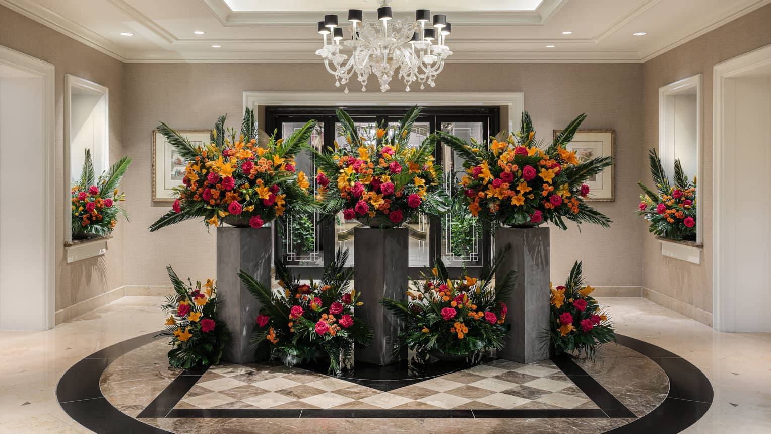 Elegant, artistic red, orange and green floral arrangements adorn a bright, spacious and neutral-toned lobby area.
