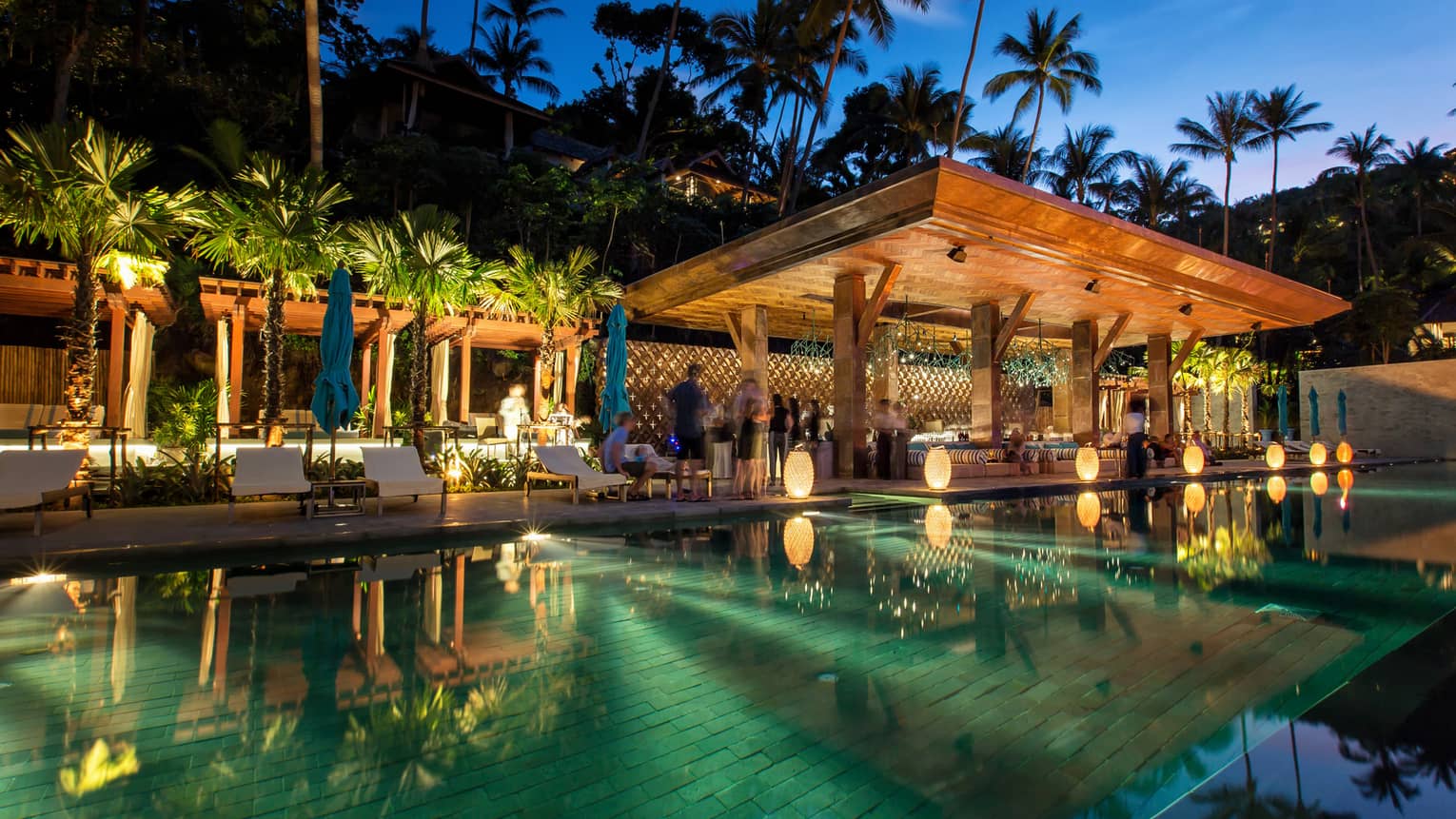 People mingle at CocoRum Bar at dusk, mirror-like pool in foreground 