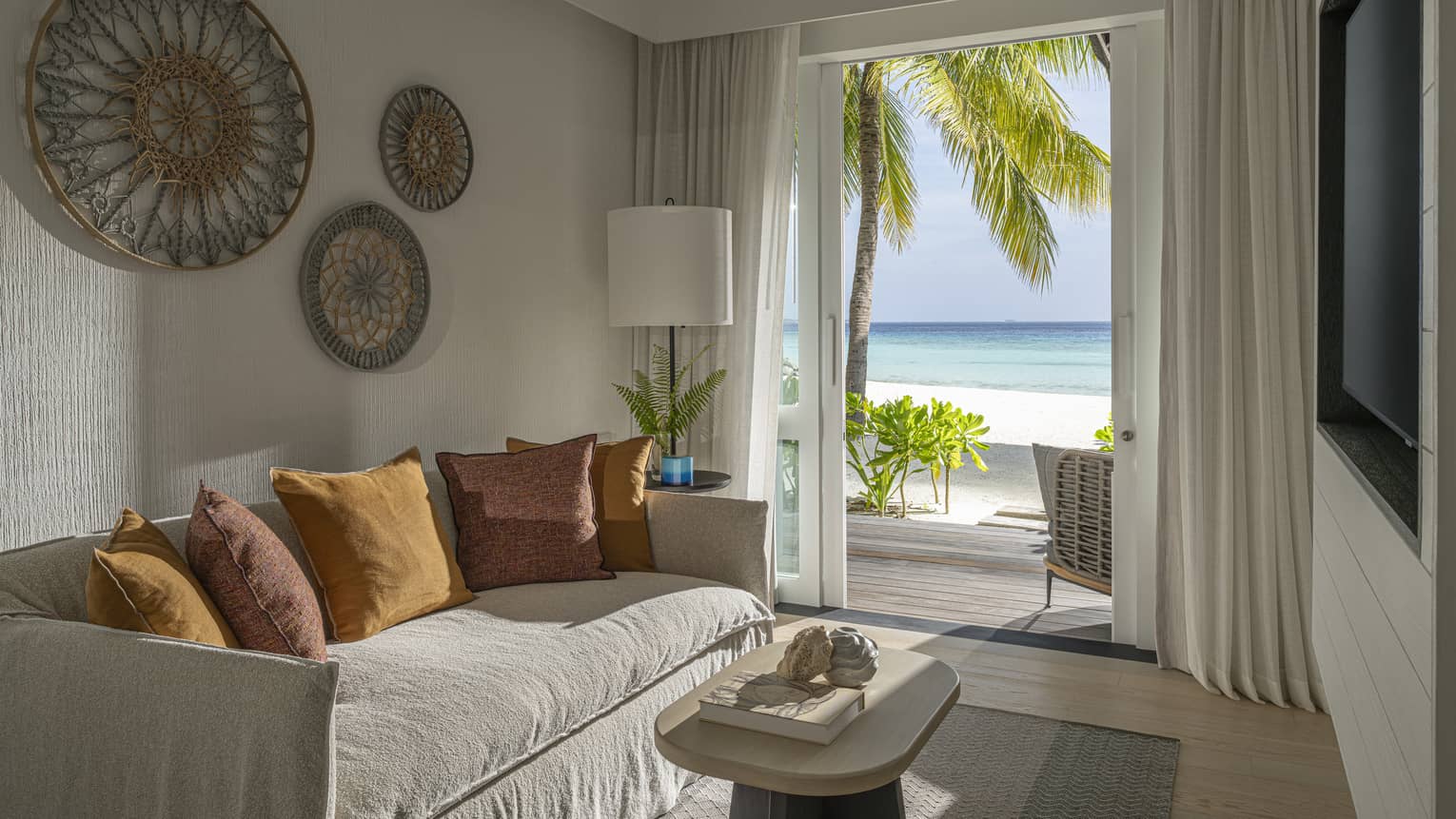 A small room with a sofa, TV, coffee table and walk-out beachfront terrace