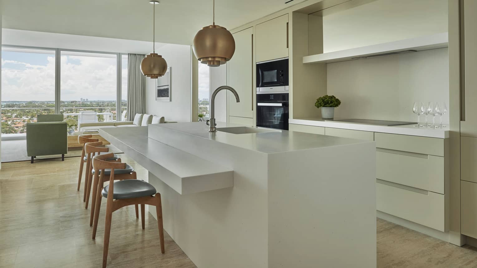 Retro-style brass lamps above white kitchen island with sink, stools