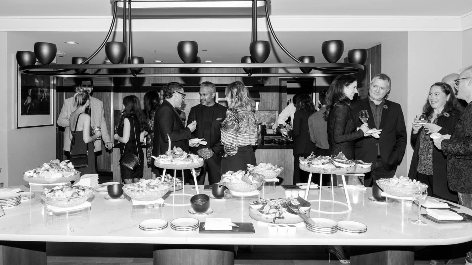 Small groups of people stand around mingling, a large oval table filled with canap�s in the foreground