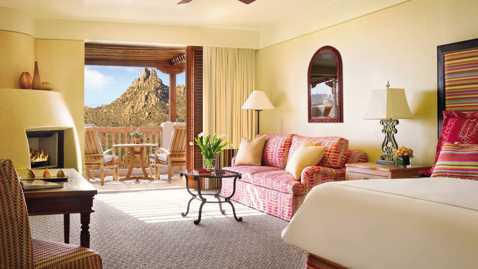 Deluxe Casita Room corner of bed, pink patterned loveseat and table by open balcony door, mountain view