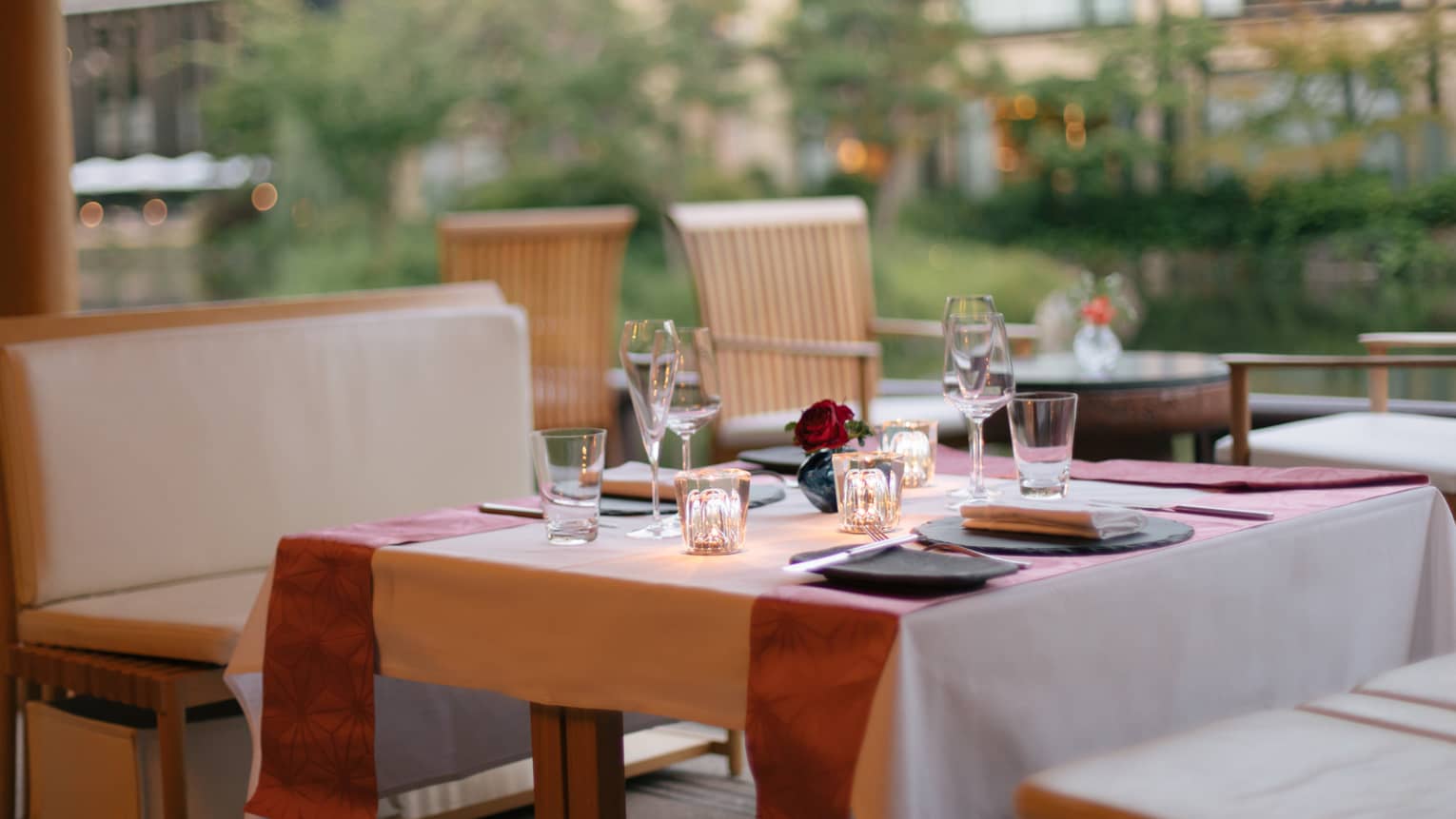Elegant outdoor dining table set with wine glasses, a small red rose centerpiece and soft lighting at Four Seasons 