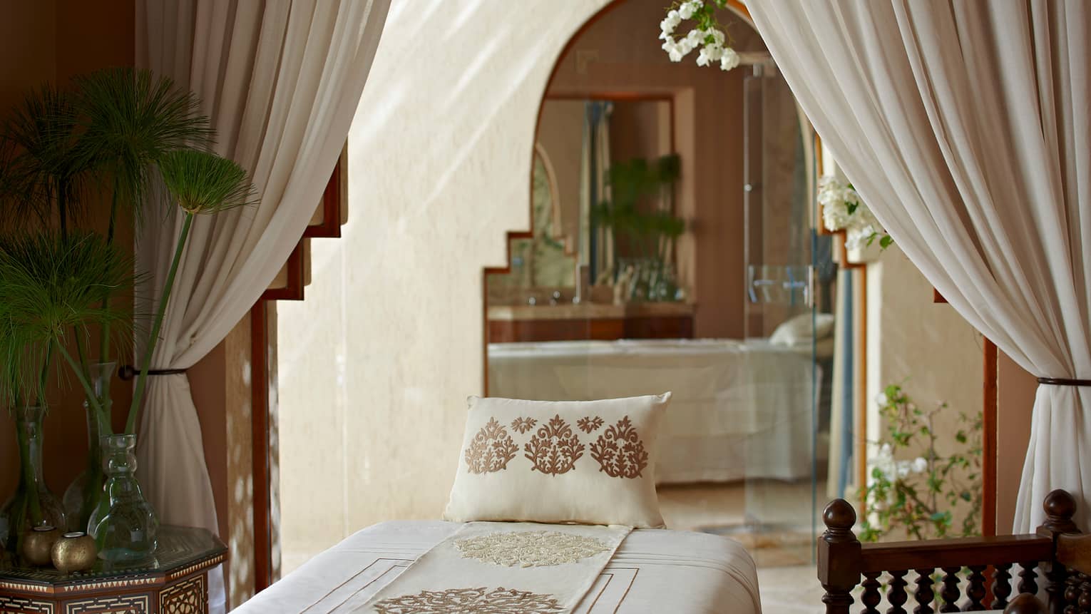 Embroidered pillow, sheet on massage table under white curtains, doorway in Spa