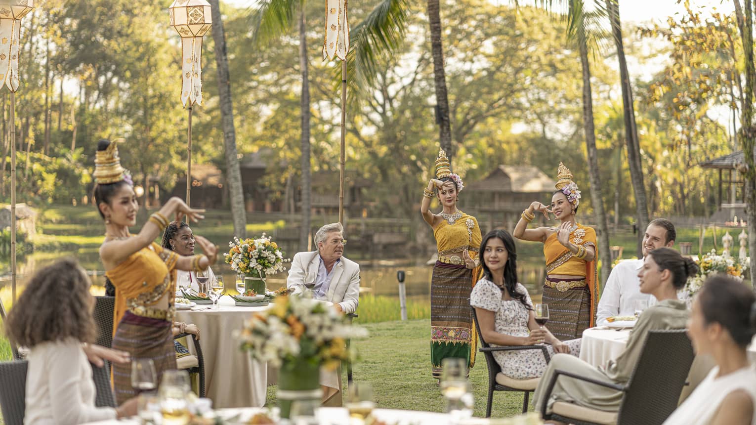 People in white sitting at various tables, as Thai dancers in yellow gowns perform in front of them.