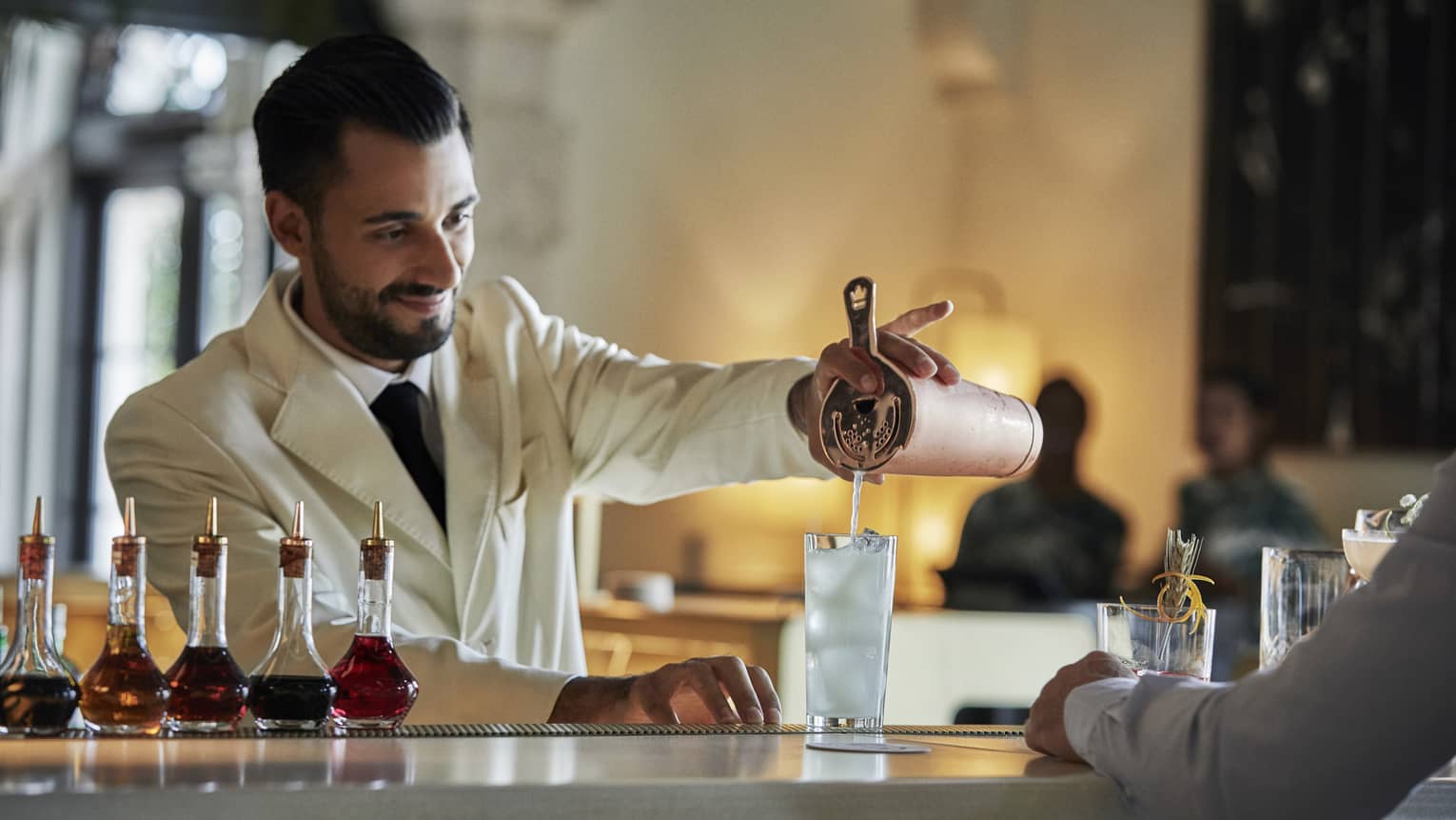 Head Bartender Valentino Longo wearing white coat pours wedding cocktail at bar