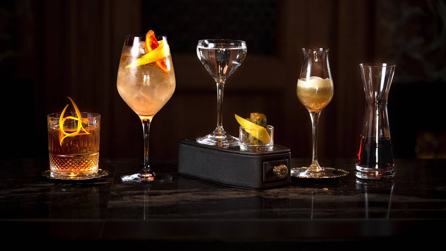 Five cocktails in different styles of glasses along dark bar 
