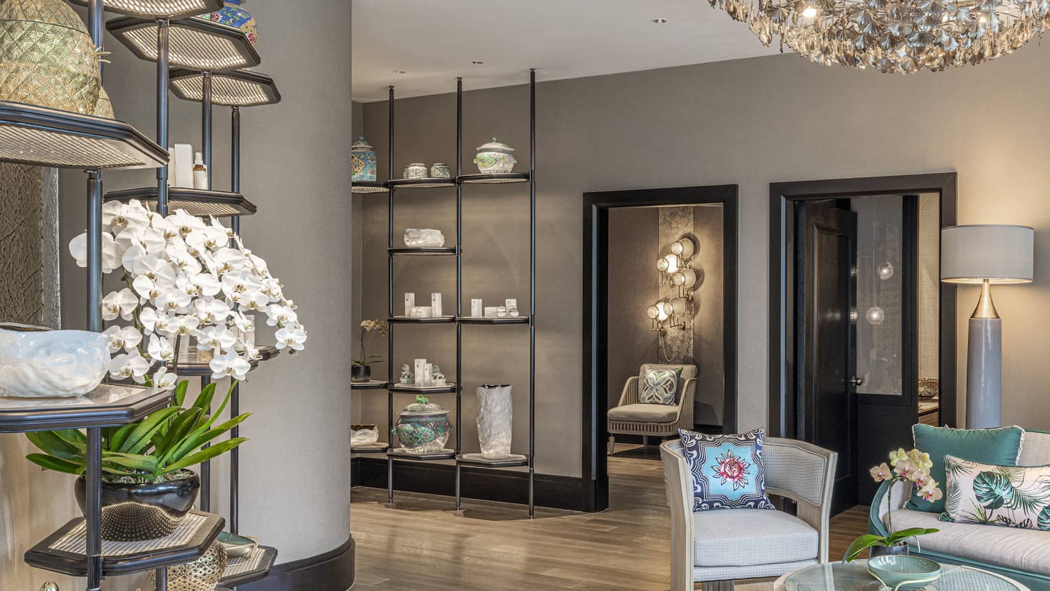 Spa lobby with cream and teal sofa, armchair, glass-top coffee table, floor-to-ceiling shelves with spa products, intimate lighting