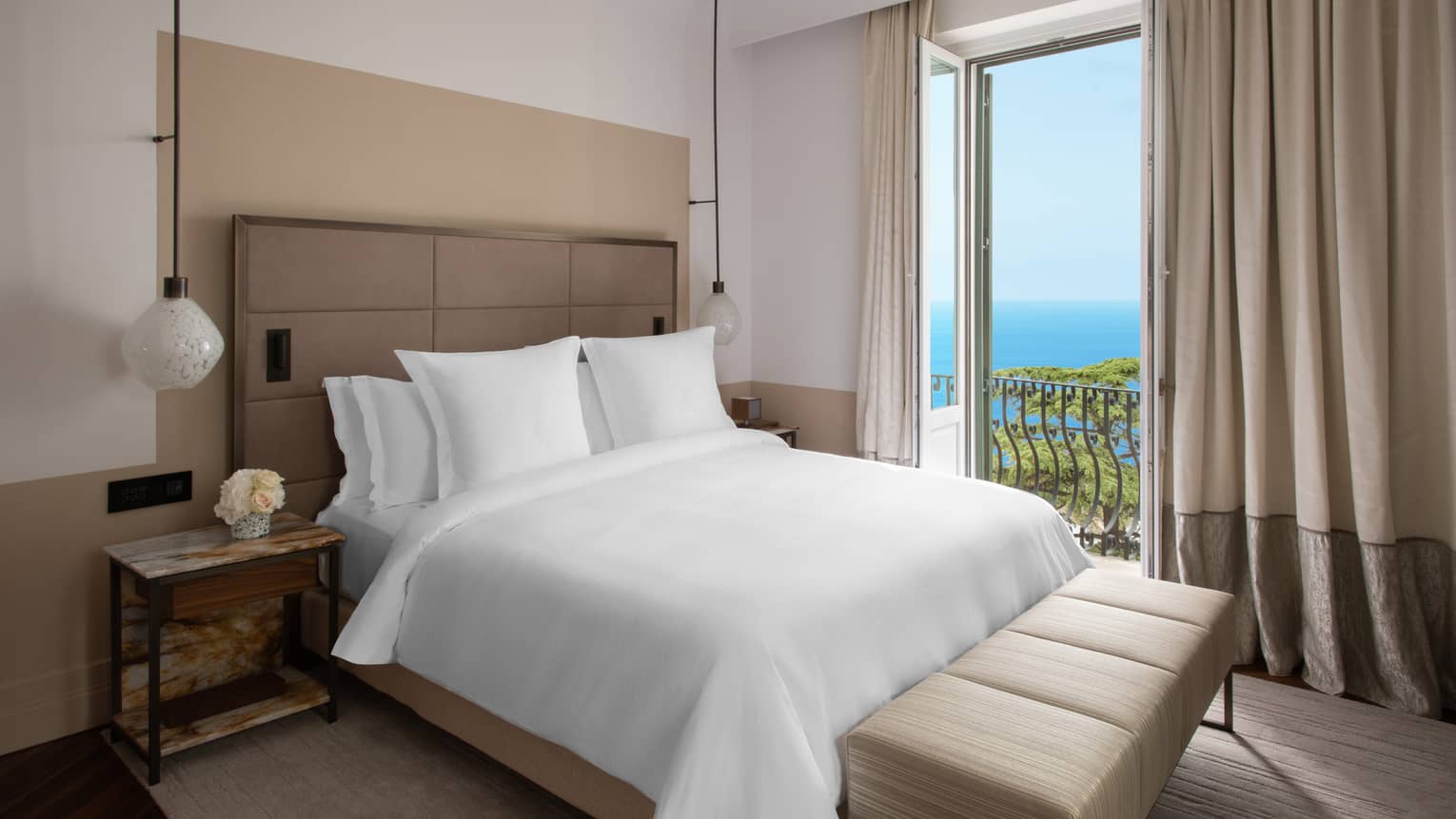 Bedroom with white king bed, full-length curtains, doors opening to sea view