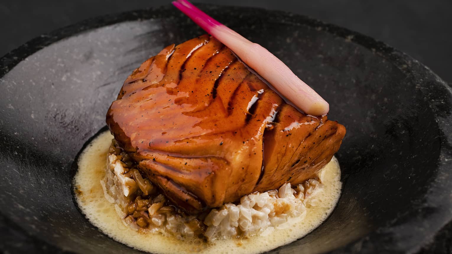 Salmon Teriyaki served atop creamy bean sprouts with teriyaki sauce in a black round bowl