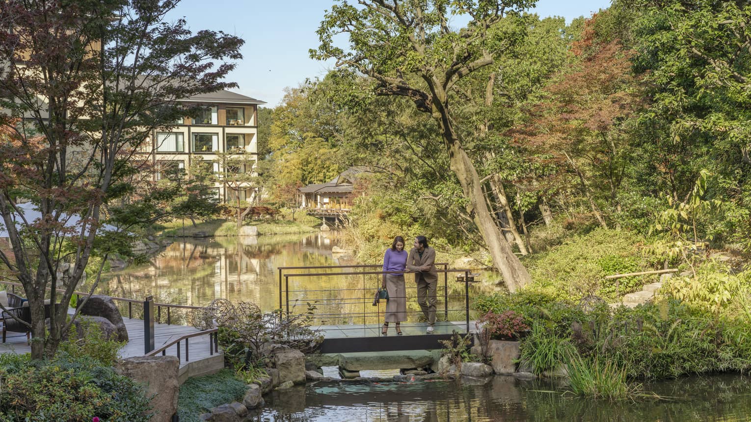 Couple stands on foot bridge overlooking koi pond
