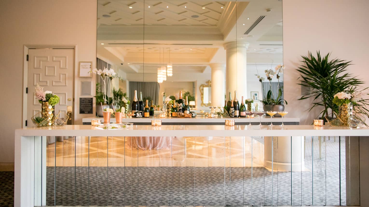 Champagne bottles on shelf under mirror behind elegant glass cocktail bar 