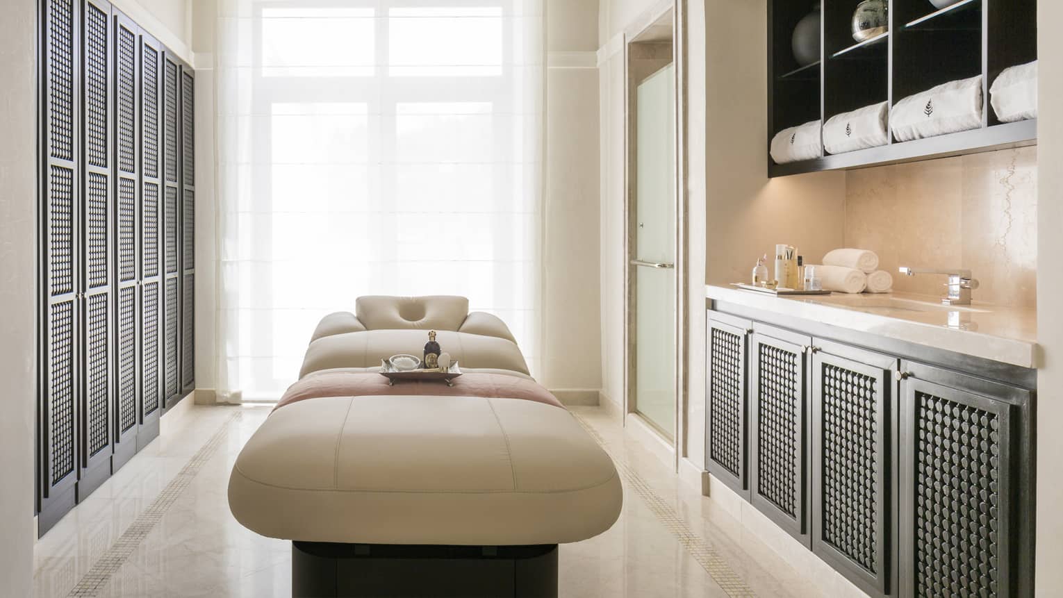 Sleek spa treatment room with white marble, black shelves, cream leather massage table 