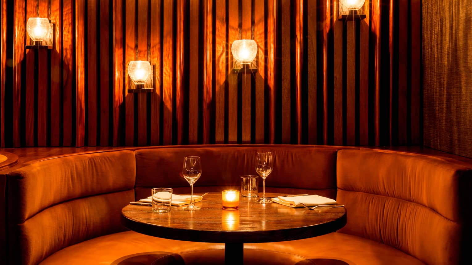 Curved plush banquette with candles, warm lights on panel wall