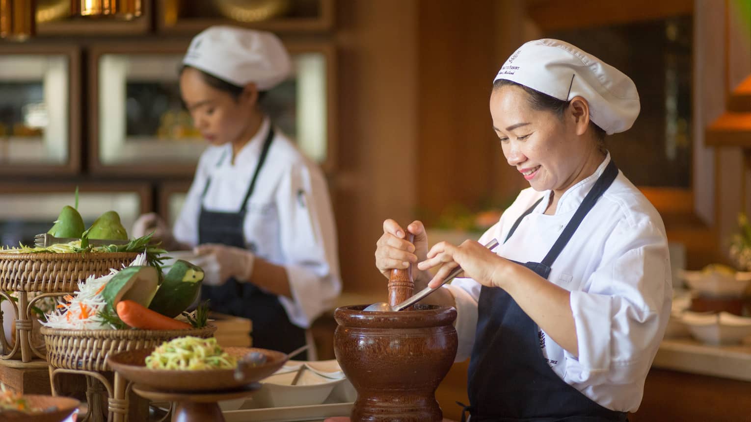Two chefs in uniform prepare authentic Thai cuisine dishes at counter with fresh vegetables