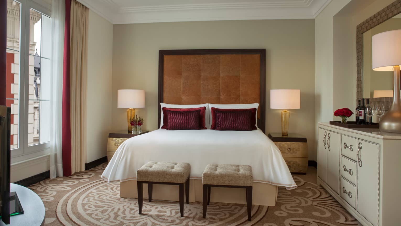 E-Lounge Junior Suite bed with tall brown leather headboard, two small plush beige stools at foot, beige patterned carpet