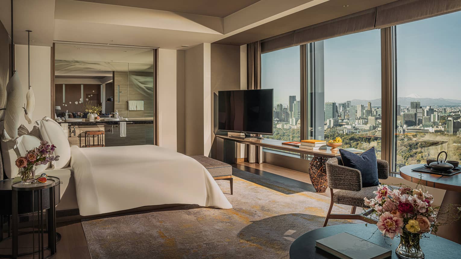 Luxury hotel suite featuring a king bed facing a wall of windows, plus a dining table