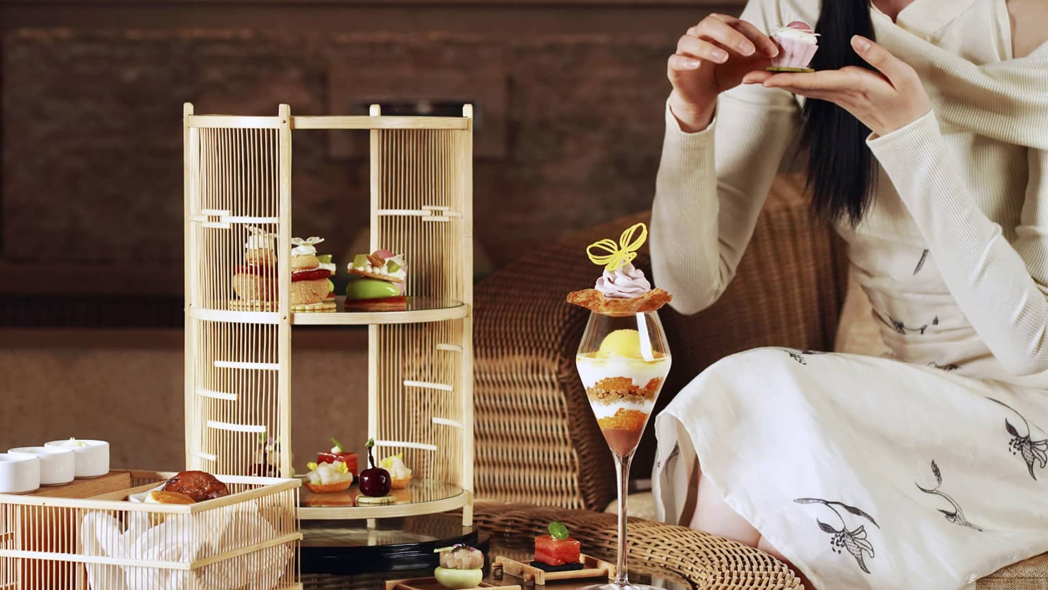 A woman sits on chair in lounge enjoying an afternoon tea spread with a tiered food display