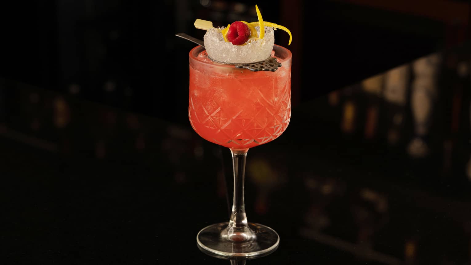 A red cocktail in a small glass with a rasberry.