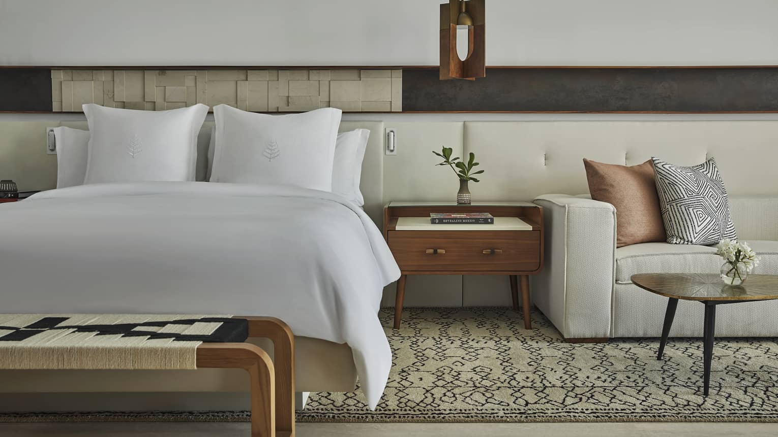 Four Seasons hotel bed, positioned next to wooden side table and sitting area with sofa