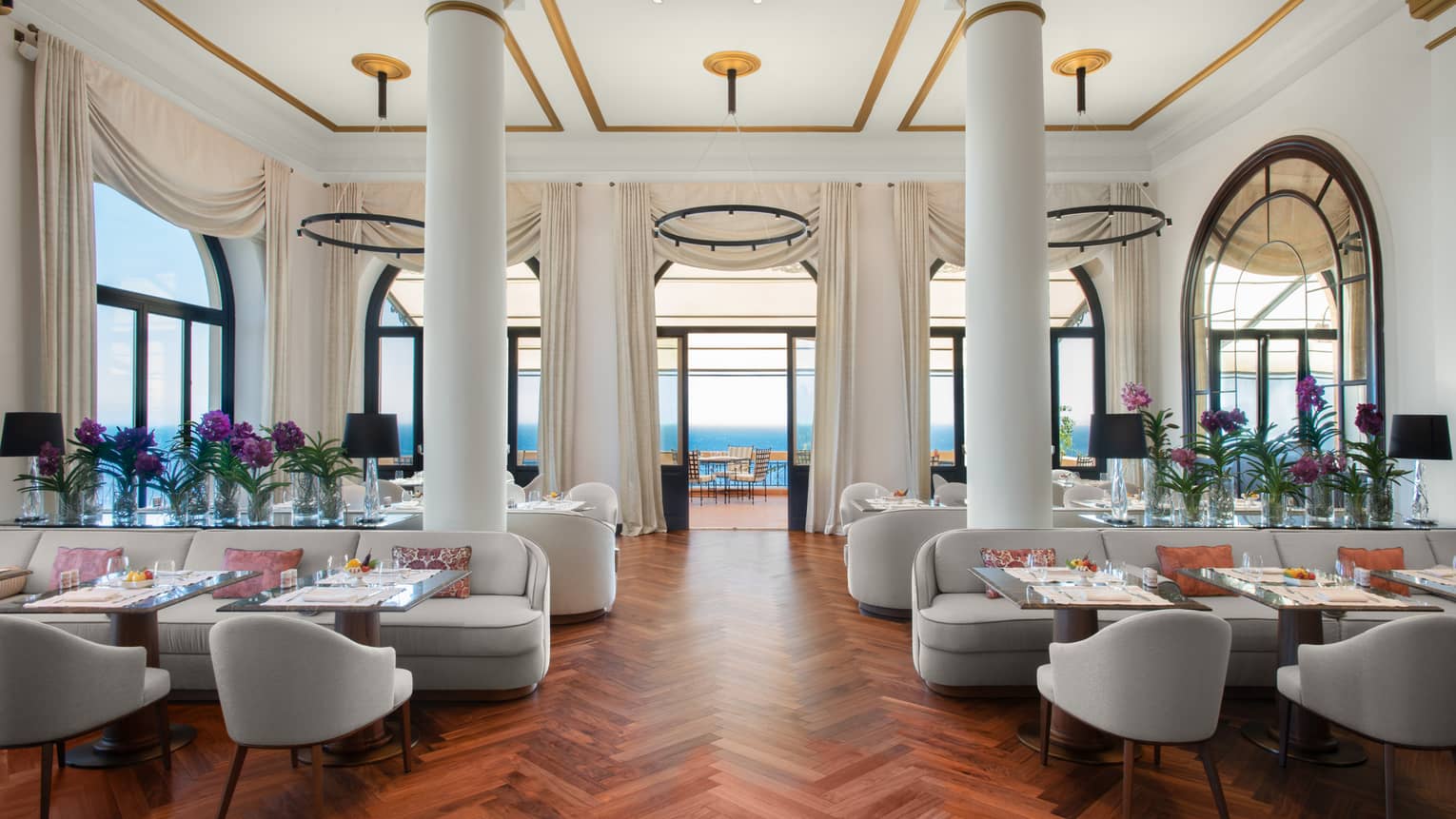 Indoor restaurant with parquet floors, two large white columns, sea view
