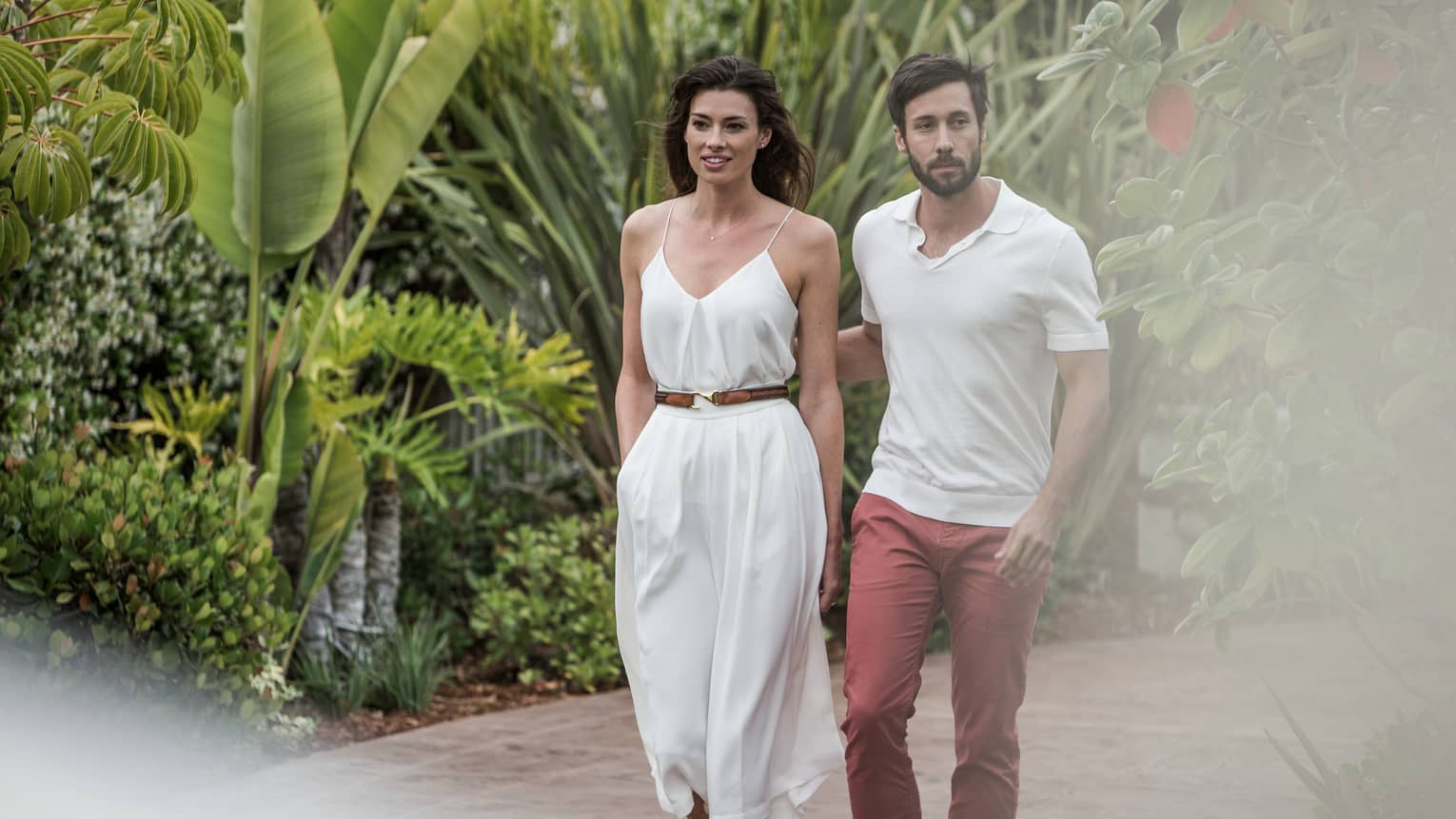 Man and woman in casual summer clothes stroll down path surrounded by tropical plants