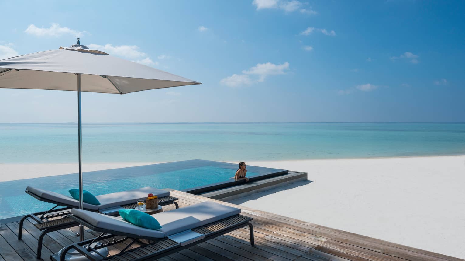 Woman leans against ledge of private infinity pool off Beach Villa patio, beach
