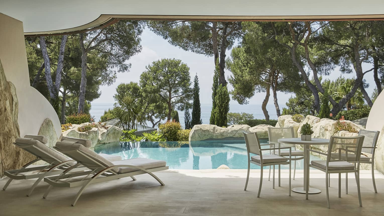 Private stone pool and terrace with two lounge chairs, table and chairs, sea view through greenery