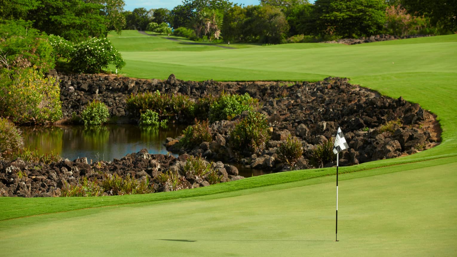 Flag, pole on golf course green near rocks, water 