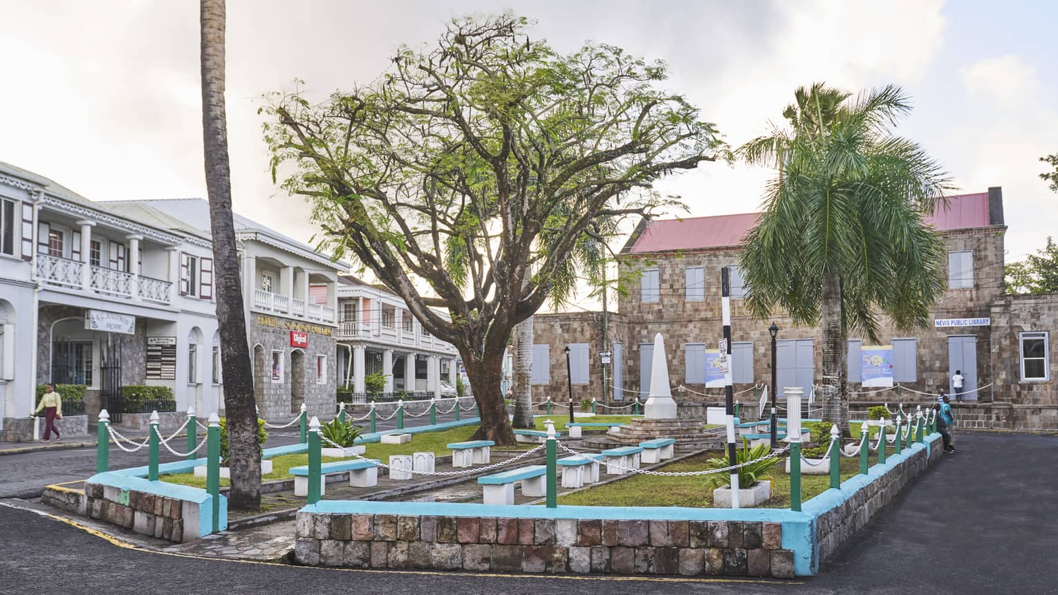 A small outdoor sitting area on a street with benches, grass and trees.