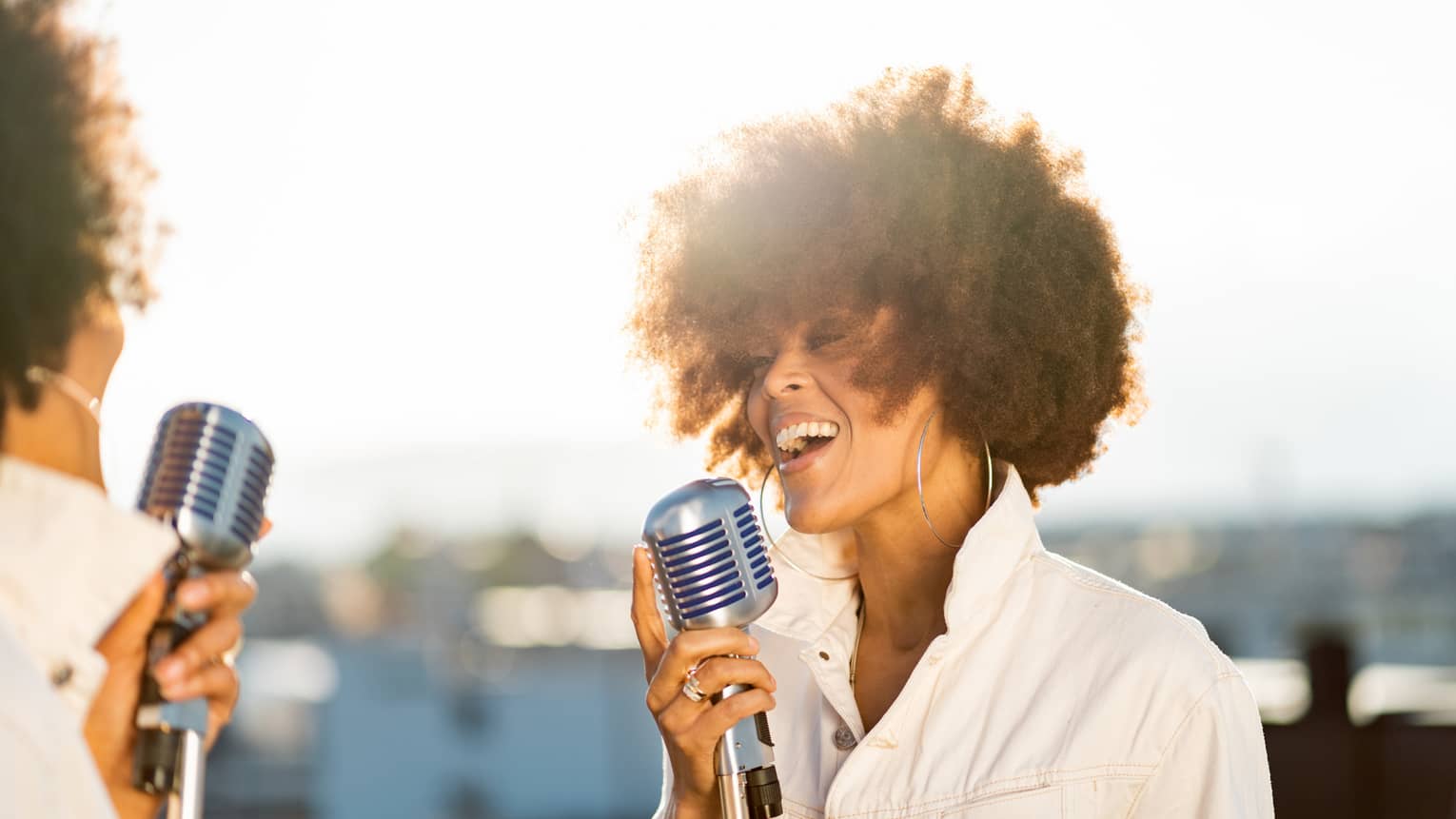 Woman wearing white jacket with collar up singing into silver retro microphone
