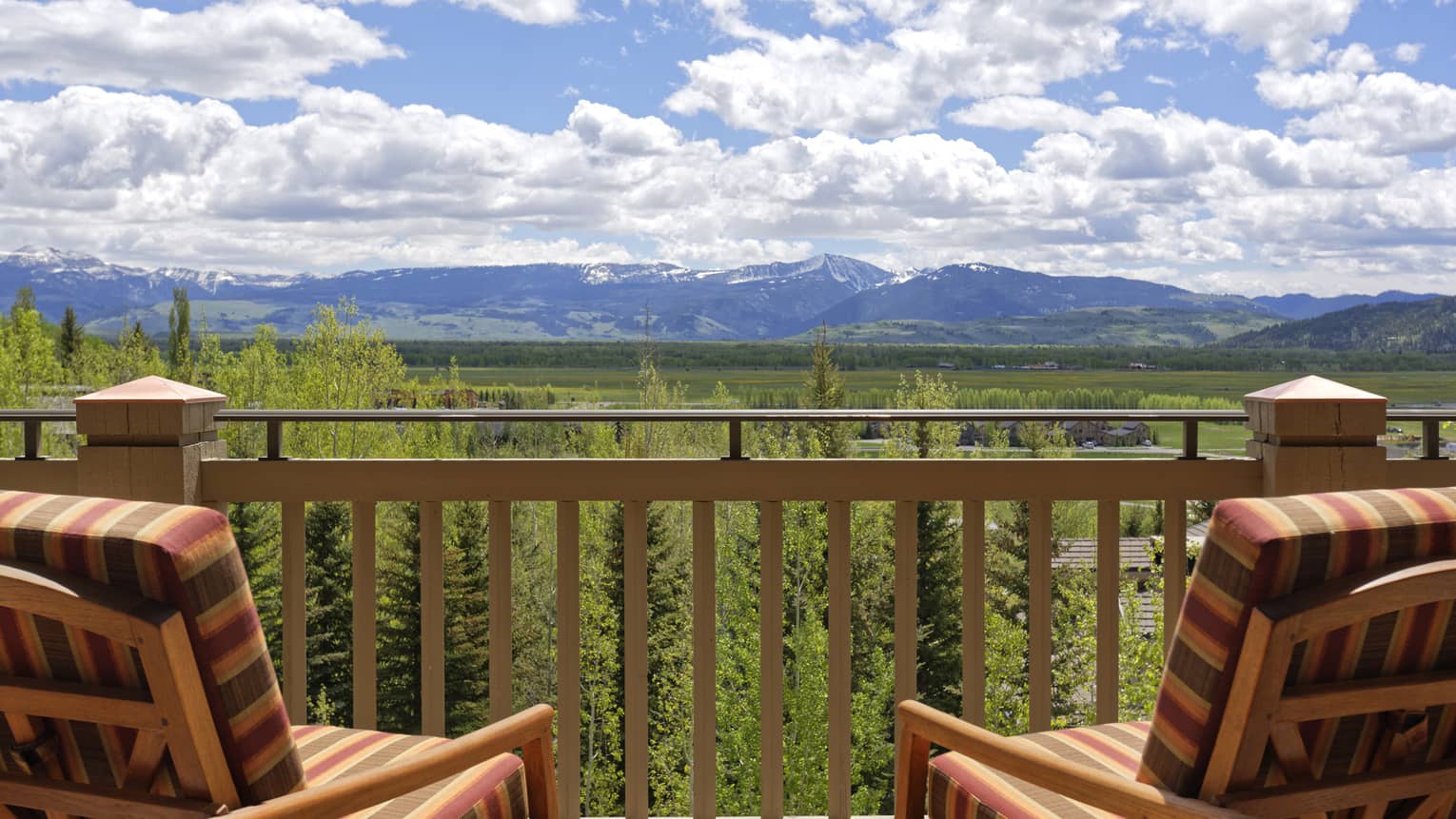 Balcony view with two striped wooden chairs overlooking a lush valley and mountains under a cloudy sky