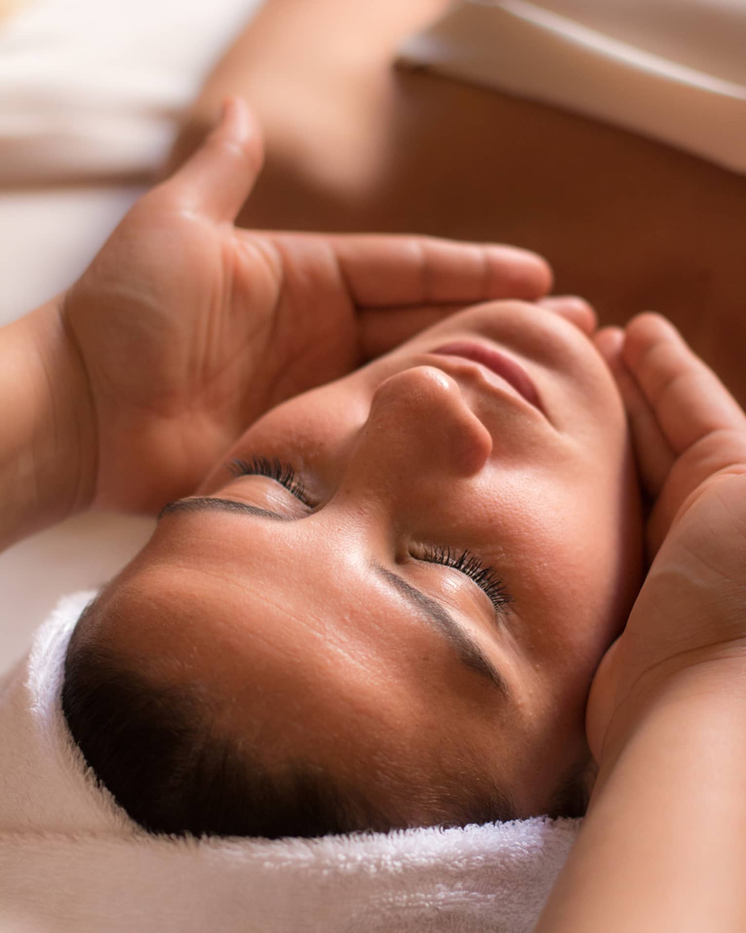 Close-up of woman with eyes closed facing up as hands cup her face and chin
