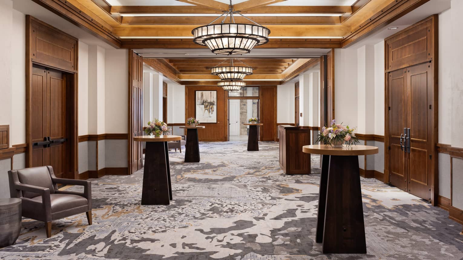 A foyer with standing tables, a large chandelier and large wooden doors.