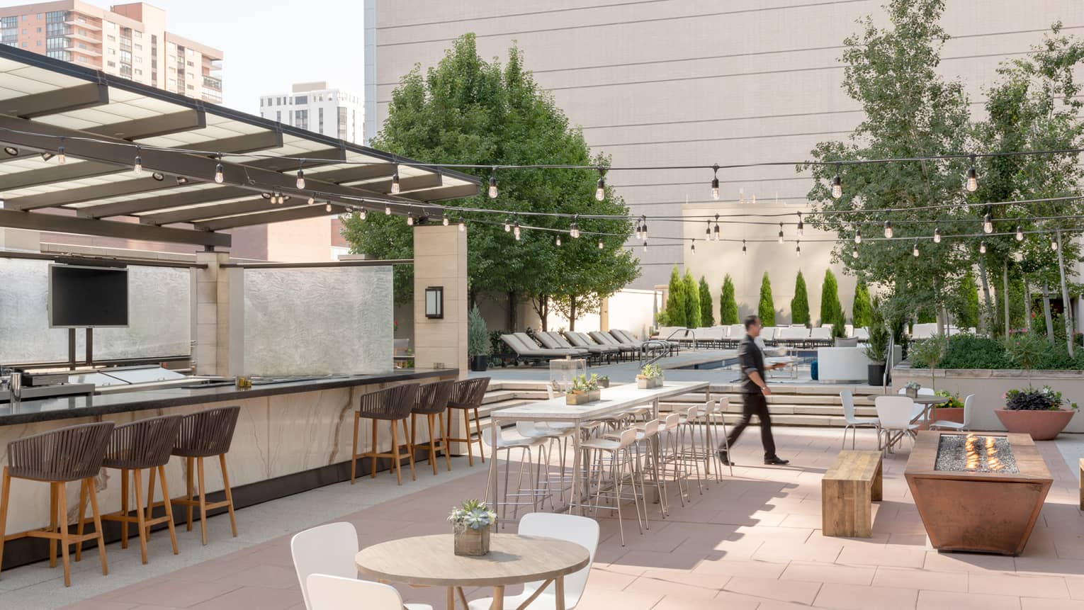 Man walks across sunny outdoor patio bar by tables, benches 