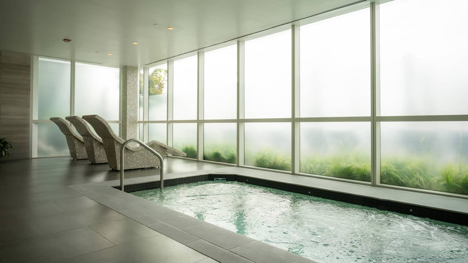 A room with three lounge chairs and a pool and floor-to-ceiling windows
