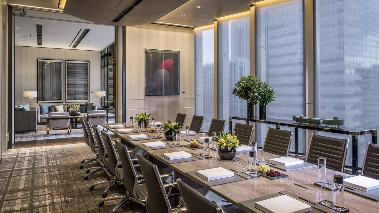 Long board table with flowers, fruit, water, lined with chairs in executive meeting suite