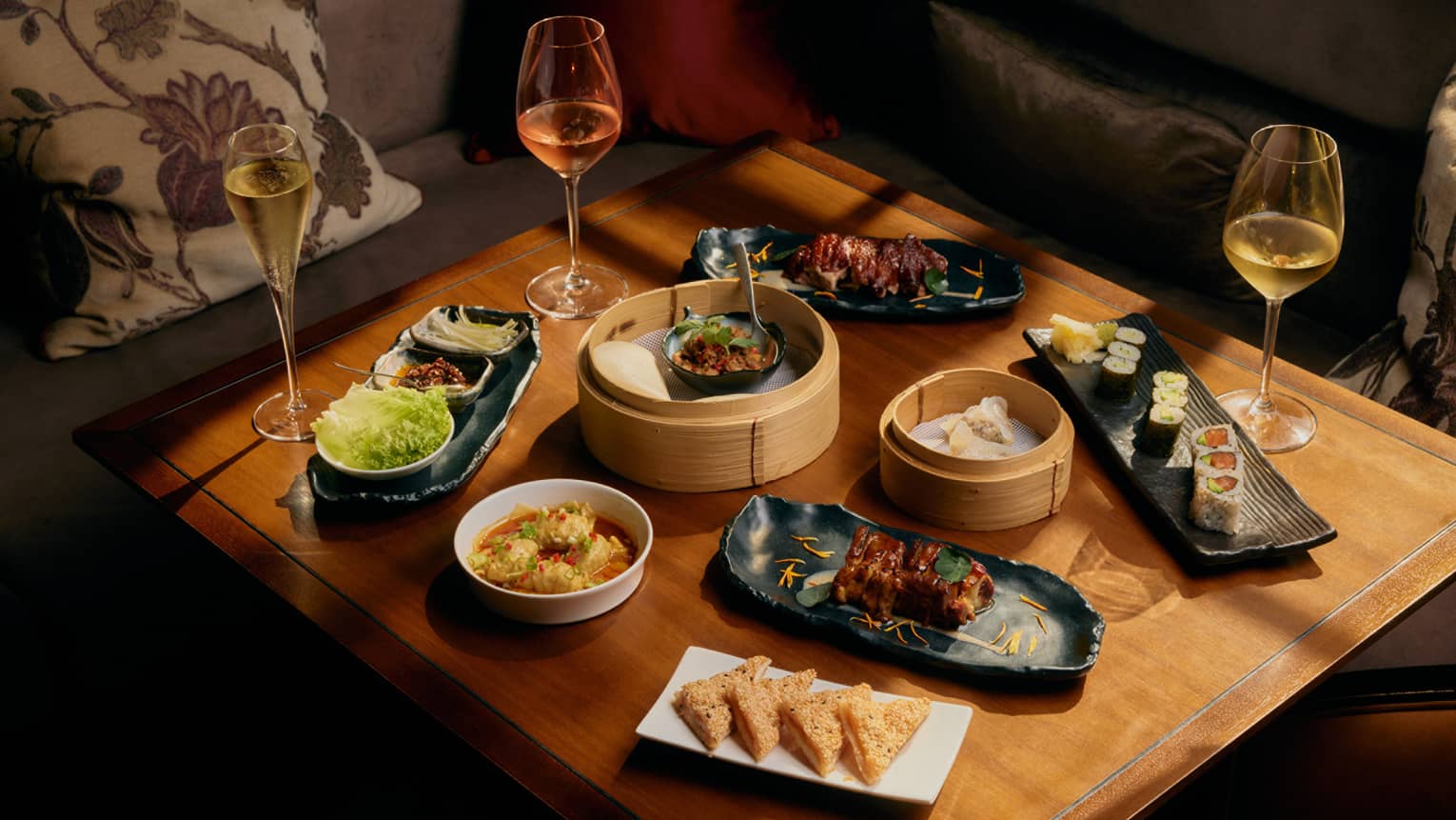 Assorted dim sum and glasses of wine on square wooden table