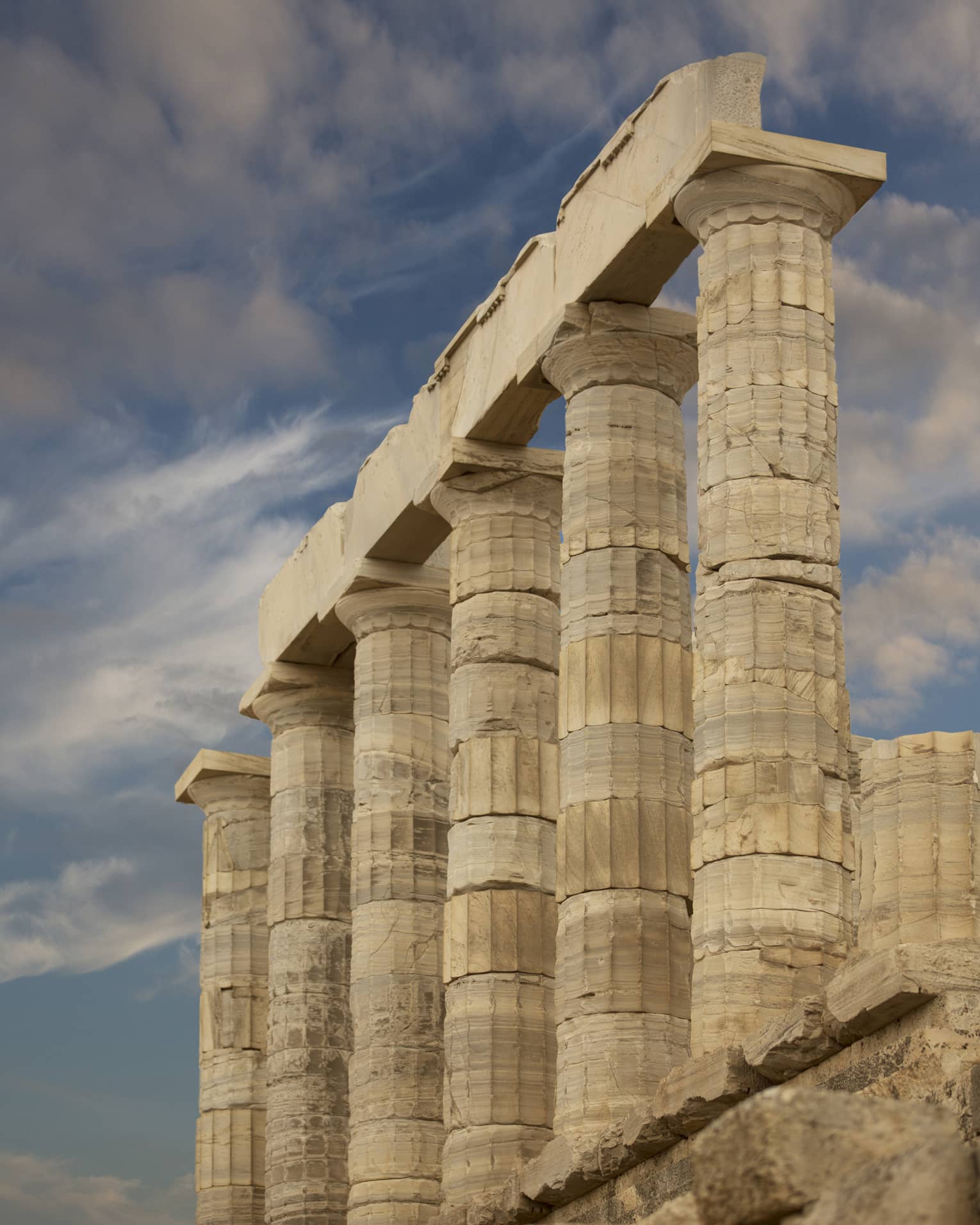 From the bottom of stairs, view of ancient towering Doric columns with vertical grooves atop a jagged brick foundation.