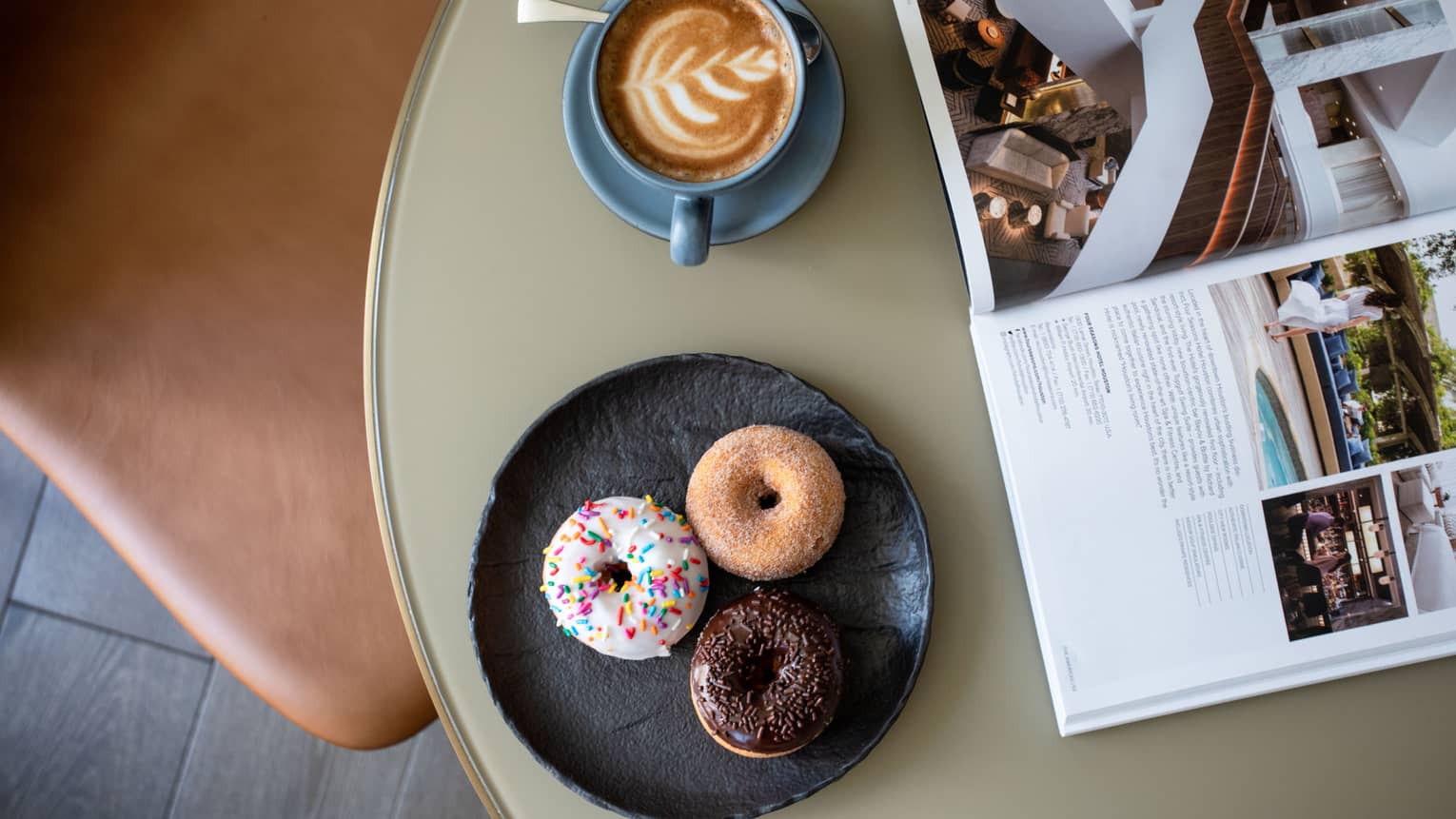 A plate of doughnuts next to coffee and an open magazine.