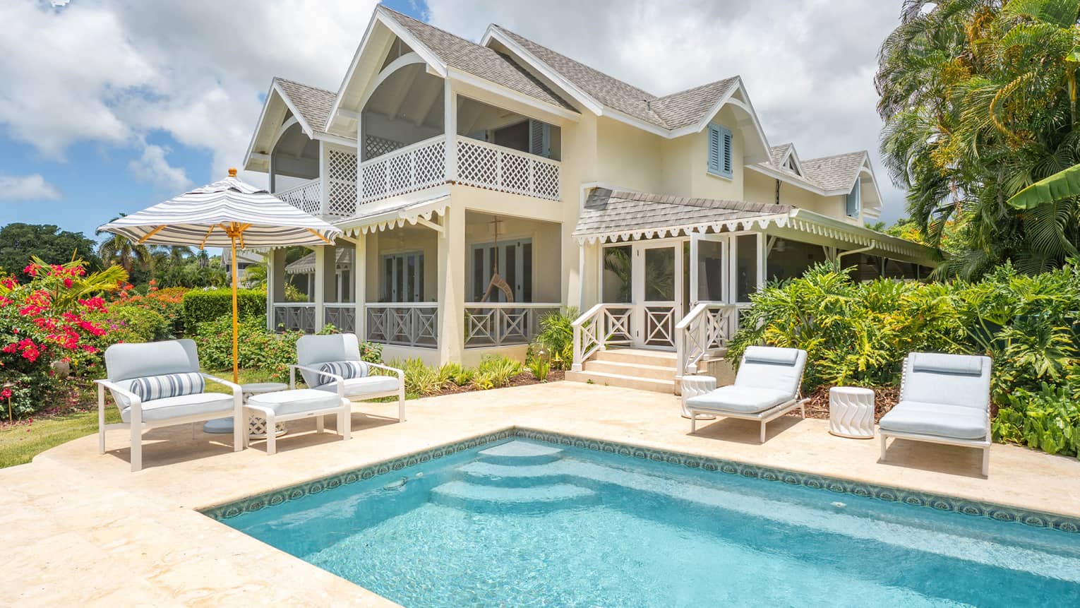 Exterior of a private residence in a tropical setting, with a large rectangular pool