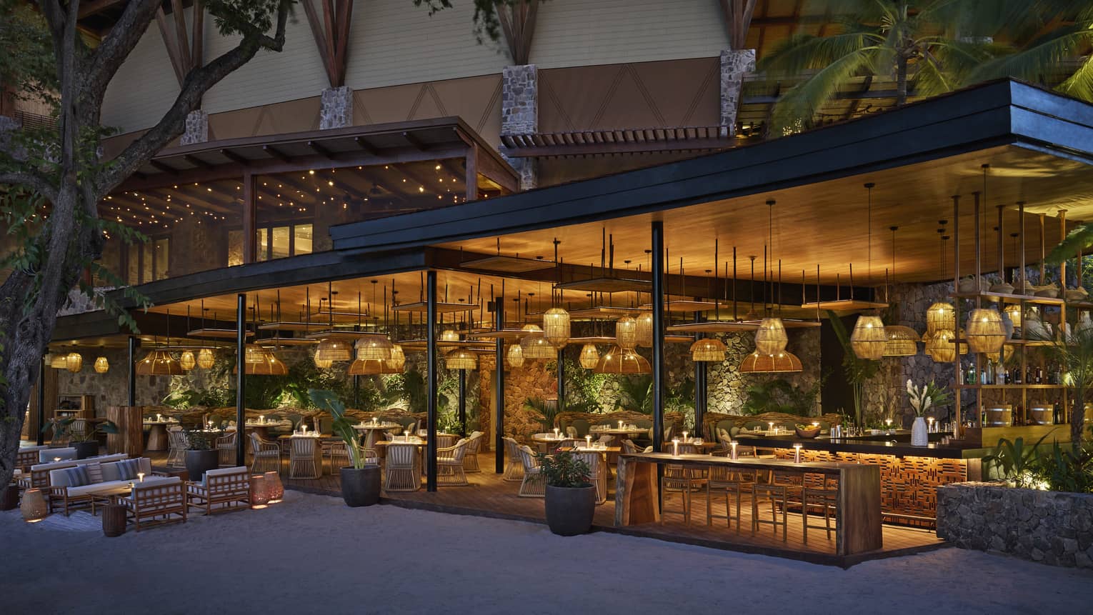 Beachside restaurant with a covered terrace featuring various hanging lanterns, multiple tables and a bar underneath