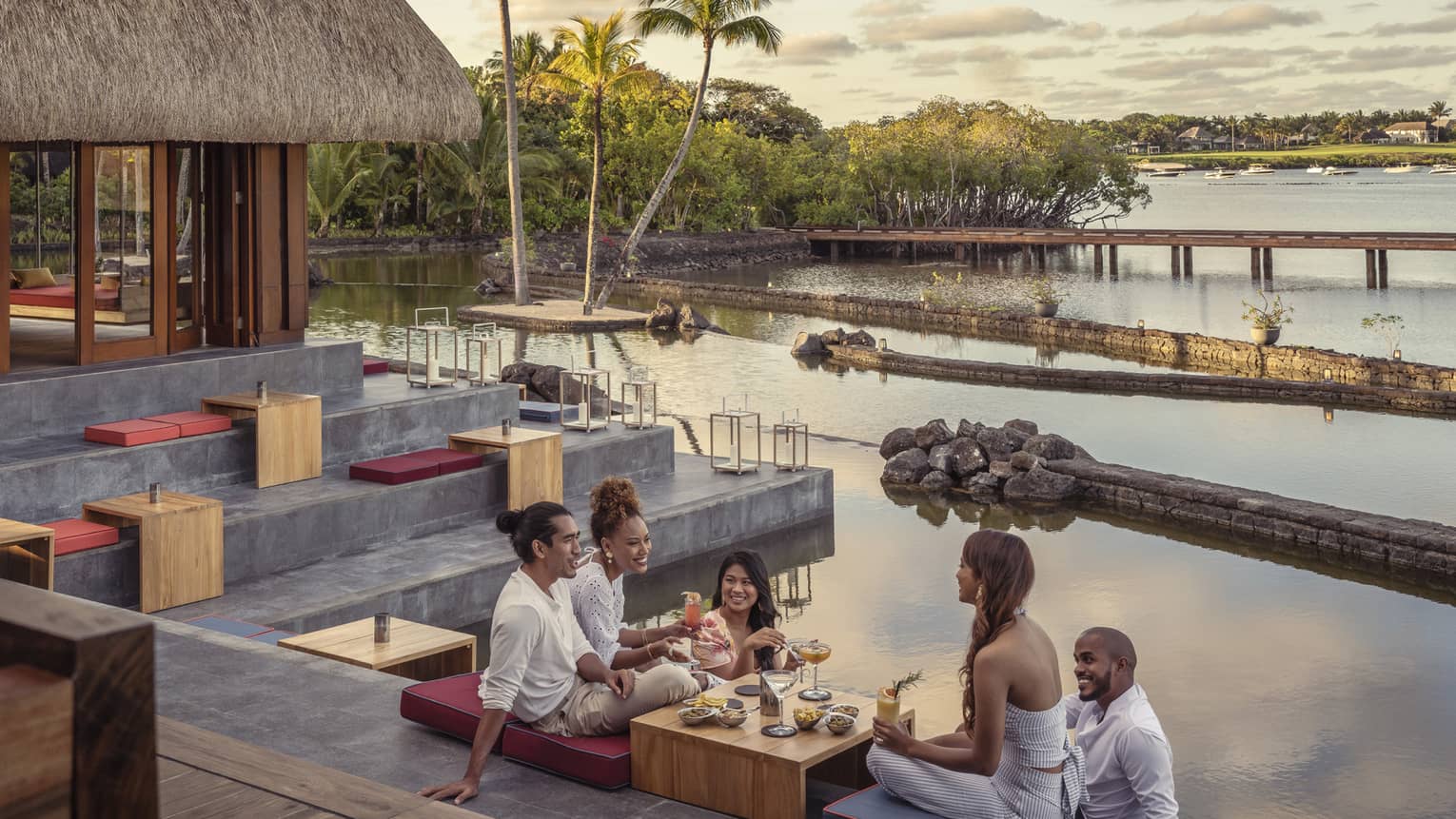 Five friends sitting and talking over food and drinks at outdoor lounge on water