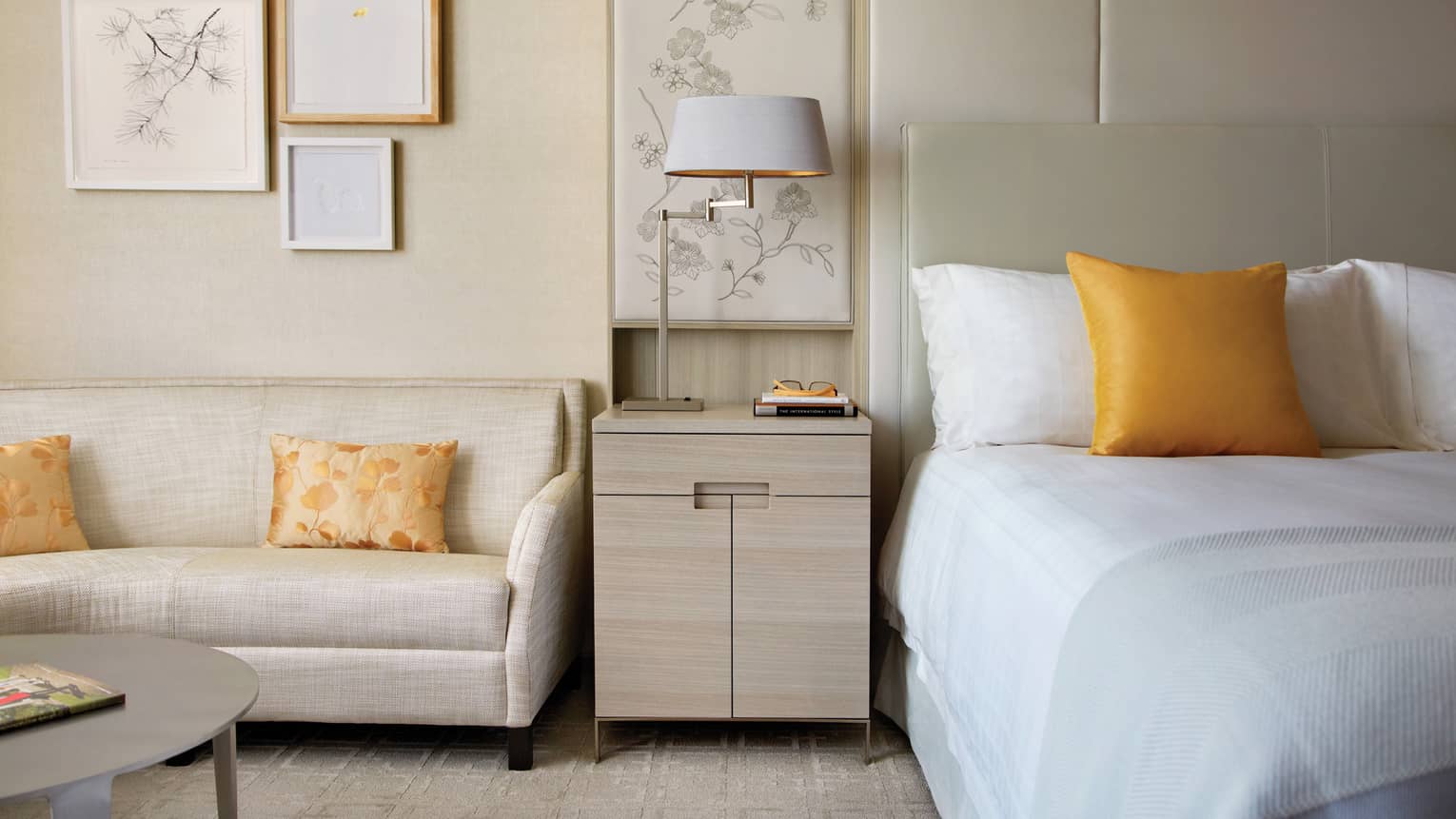 White loveseat by light wood nightstand, bed with golden yellow accent pillow
